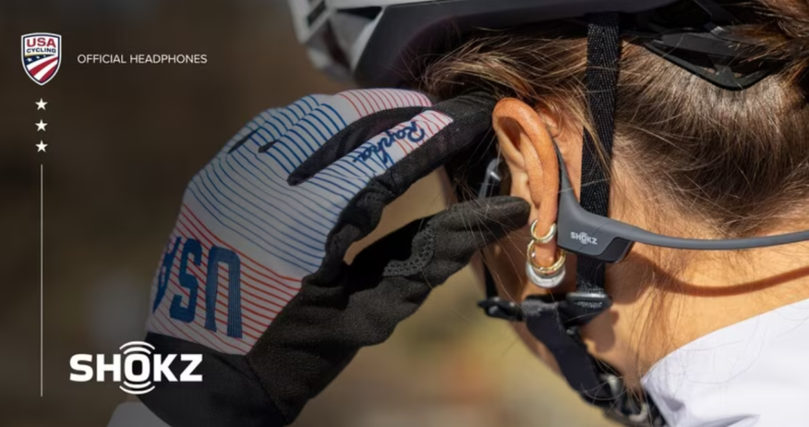 Femme cadre pratiquant le cyclisme avec des écouteurs à conduction osseuse dans un environnement urbain moderne.